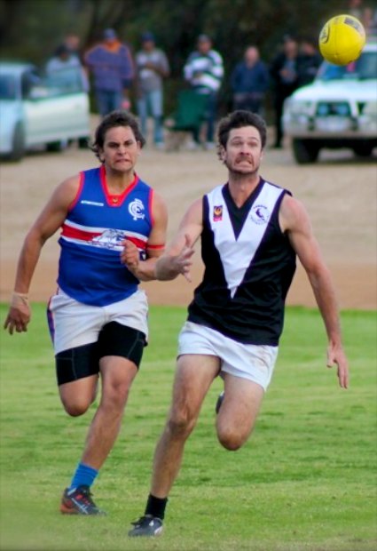 Two Australian rules football players chasing a ball.